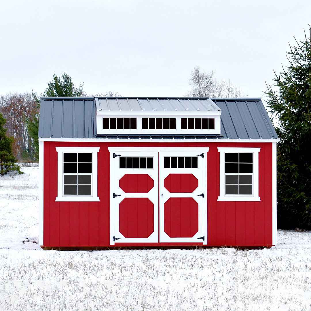 Red Utility Shed with white trim and dormer windows, featuring a gray metal roof, set against a snowy winter landscape.