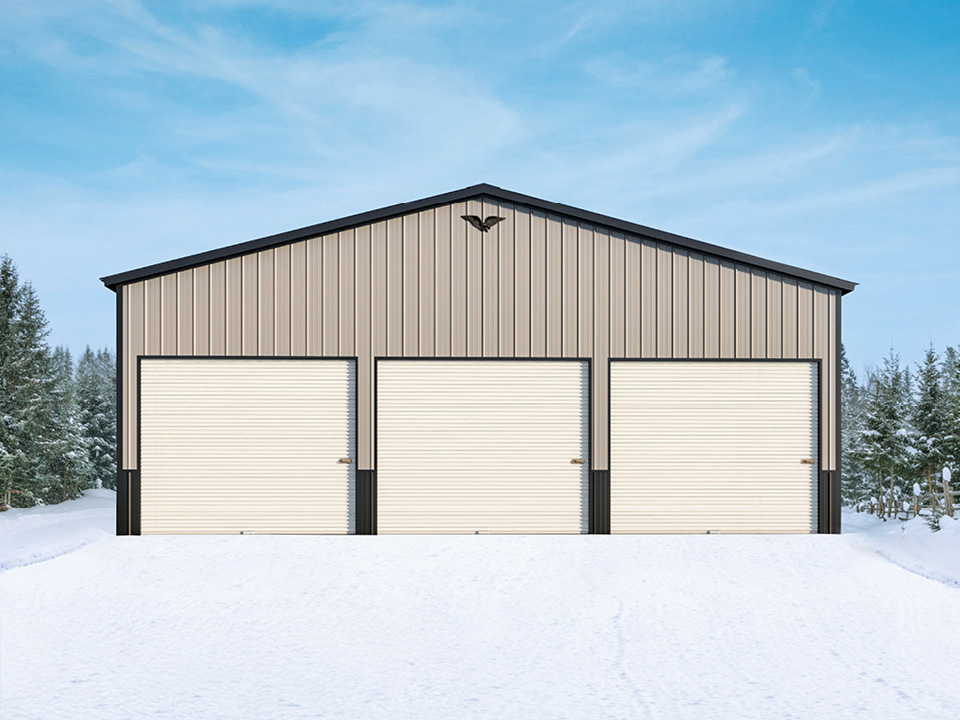 Large metal building with three roll-up garage doors, tan siding, black trim, and an eagle emblem at the peak, set against a snowy landscape and a clear blue sky.