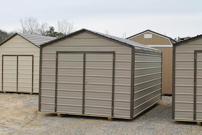 Tan utility shed with burnished slate trim displayed on a gravel lot, surrounded by additional storage shed options.